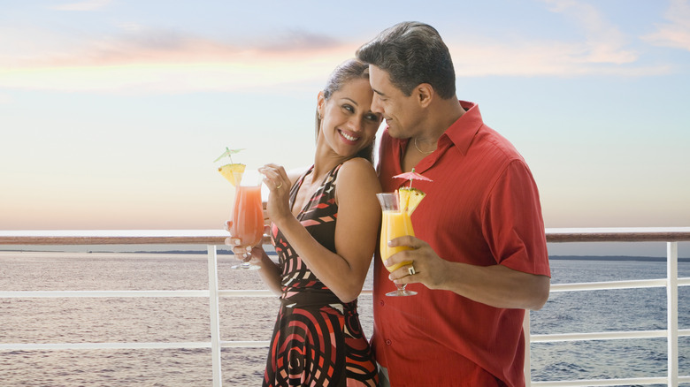 A man and woman hold cocktails on the deck of a ship